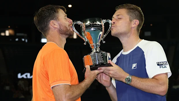 Neal Skupski (R) da Grã-Bretanha e Christian Harrison (L) dos Estados Unidos beijam o troféu após a final de duplas masculinas contra Jason Kubler e Marc Polmans da Austrália durante o dia 14 do Aberto da Austrália de 2026 em Melbourne Park em 31 de janeiro de 2026 em Melbourne, Austrália. (Foto de Clive Brunskill/Getty Images)