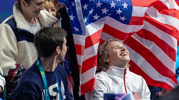 Ilia Malinin reage com seus companheiros conforme sua pontuação aparece após realizar sua rotina.