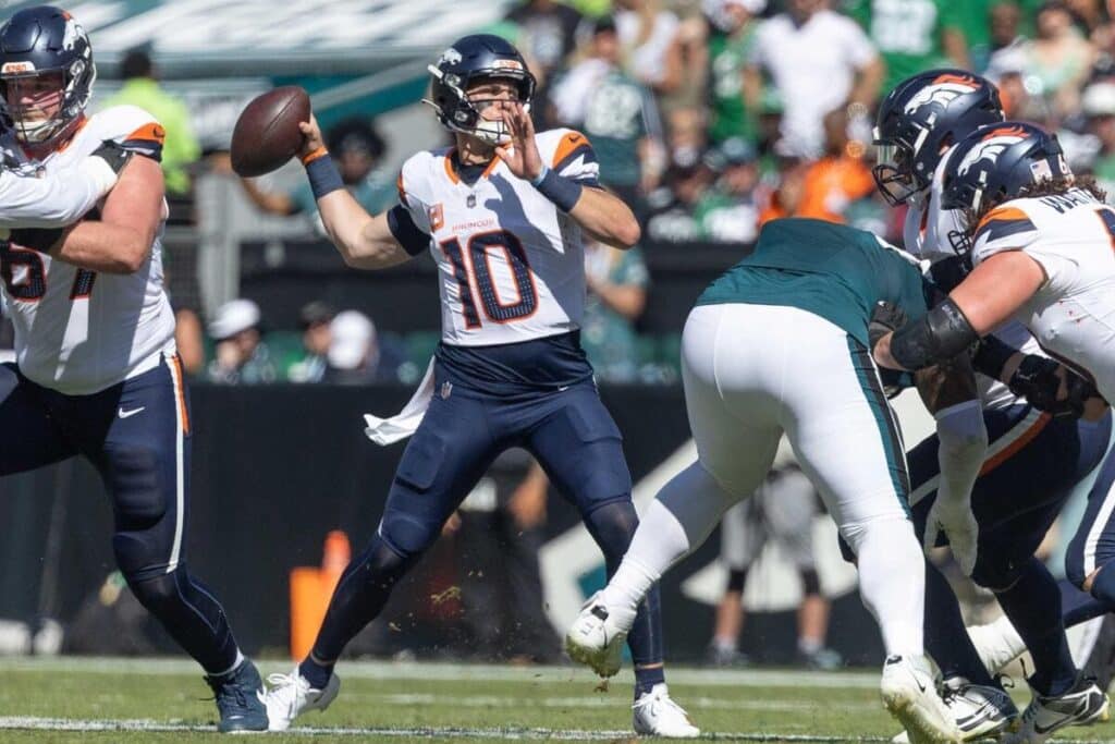 O quarterback do Denver Broncos, Bo Nix, jogando uma bola de futebol durante um jogo.