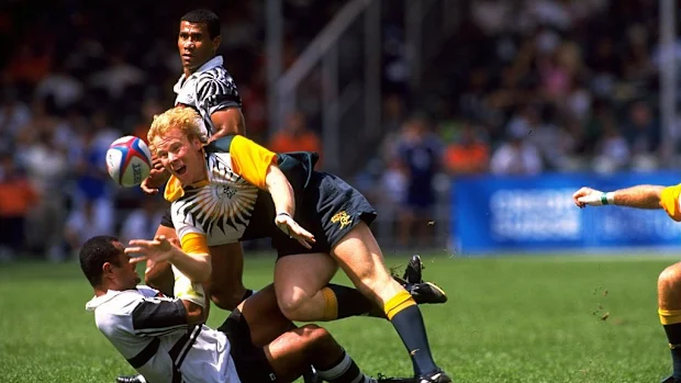 Um jogador australiano é jogado ao chão por um jogador de Fiji no Hong Kong Rugby Sevens de 1998.
