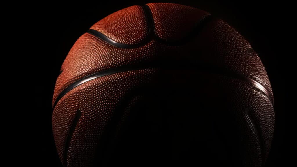 Um close de uma bola de basquete da NBA nas sombras. A bola é laranja escura com linhas pretas