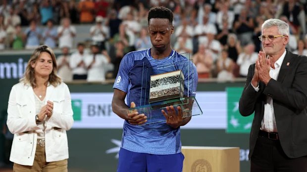 PARIS, FRANÇA - 25 DE MAIO: Gael Monls da França é presenteado com um troféu contendo argila e solo de Roland Garros por Amelie Mauresmo - Diretora do Torneio, e Gilles Moretton - Presidente da Federação Francesa de Tênis, após derrota para Hugo Gaston da França em sua primeira rodada de Singles Masculinos no segundo dia do Aberto da França de 2026 em Roland Garros em 25 de maio de 2026 em Paris, França. (Foto de Dan Istitene/Getty Images)