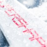 Close-up of the SUPERSHAPE lettering on a white HEAD ski topsheet covered in fresh snow