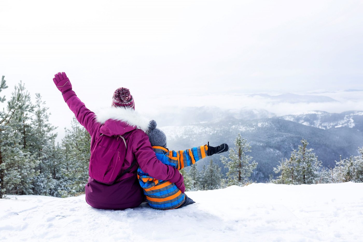 Pai e filho sentados na neve olhando para as montanhas em férias de esqui em família